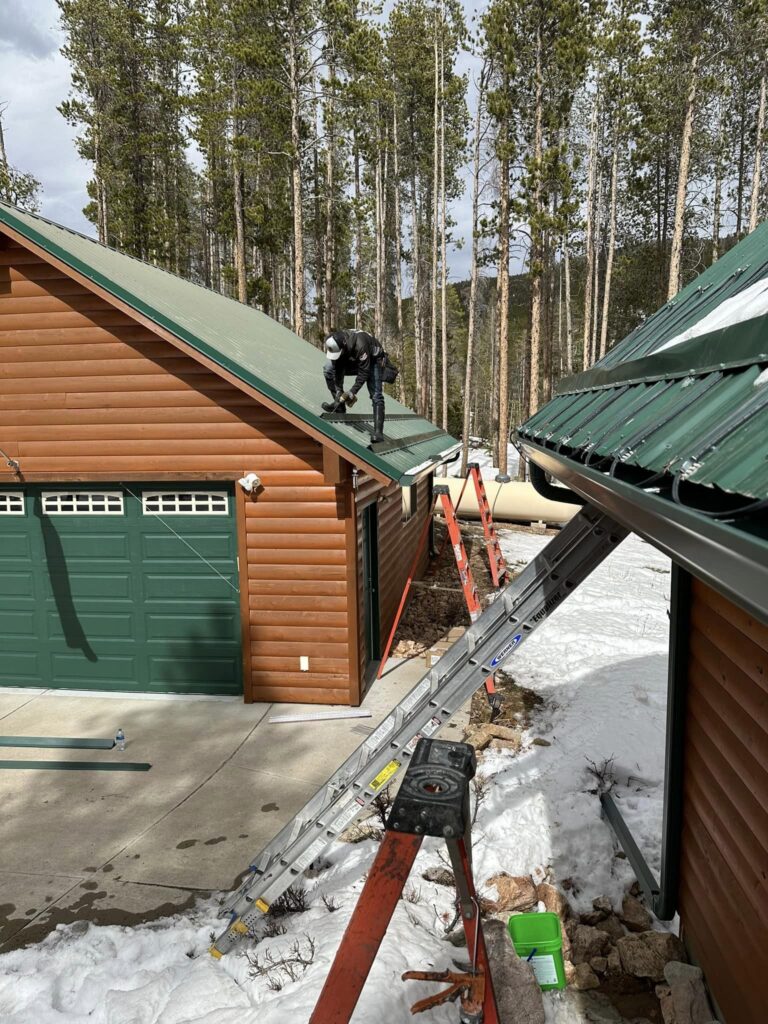 C&S Rain Gutters crew member on a metal roof in snow, with heat cable run in a zigzag along the roof edge